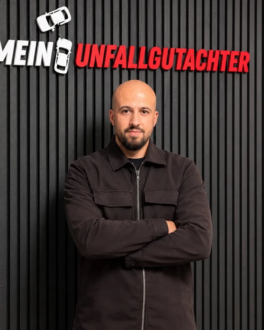 Hamit Günaltay, Geschäftsführer bei Mein Unfallgutachter, vor der Logo-Wand im Büro